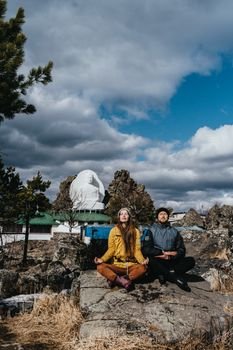 A couple sitting in meditation pose outdoors near a large Buddha statue. Calm and tranquil setting.