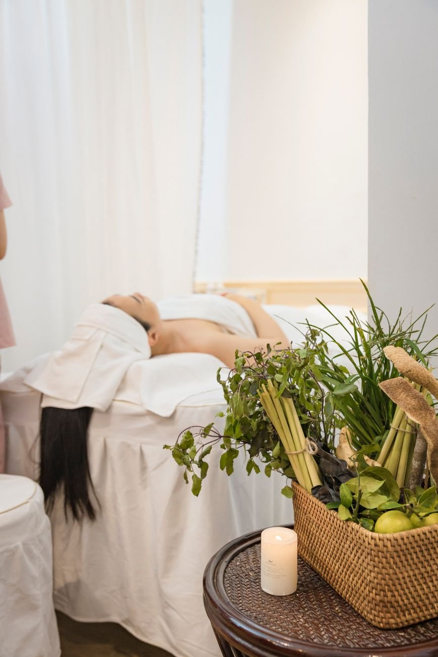 A serene spa setting featuring a woman receiving a relaxing massage with aromatic herbs nearby.